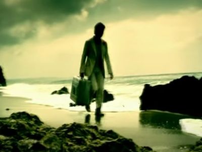 A man is walking on a beach in a suitcase holding a briefcase.